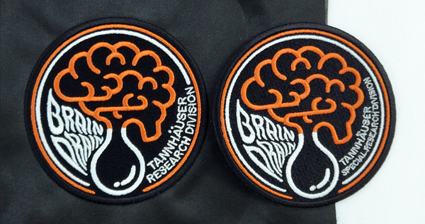 Two Brain Drain patches side by side, each with slightly different designs and text.
